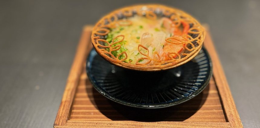 Bowl of soup with crustacean and decorated with pastry on a wooden board.