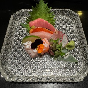 Sashimi and greens on a glass plate.